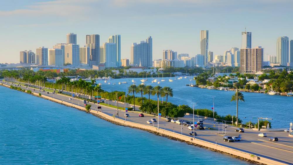 Vista panorâmica de Miami com rodovia sobre águas cristalinas e arranha-céus ao fundo, representando o cenário ideal para investimento imobiliário de luxo na Flórida.